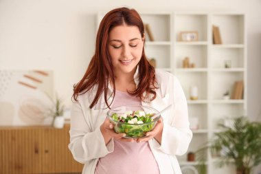 Evde taze sebze salatalı hamile bir kadın var.