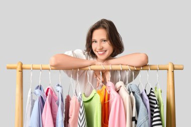 Beyaz arka planda farklı giysileri olan, rafların yanında güzel genç bir kadın.