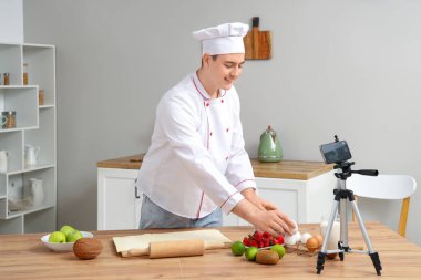 Hamurlu erkek aşçı mutfakta yemek pişirme videosu kaydediyor.