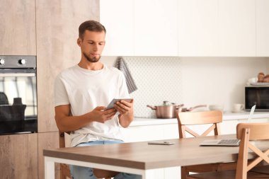 Genç adam mutfakta akıllı ev kontrol paneli kullanıyor.