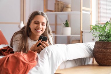 Yatak odasında cep telefonu kullanan güzel bir genç kadın.