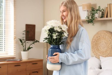 Evinde bir buket beyaz kasımpatı çiçeğiyle güzel, genç, mutlu bir kadın.