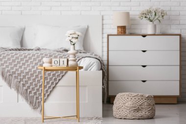 Küp takvimli masa, çiçekler ve mum şık bir yatak odasında.