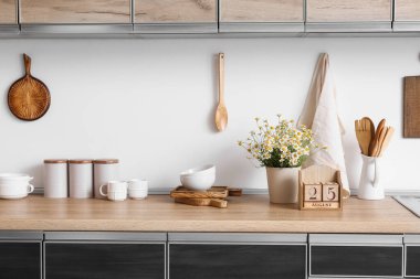 Mutfaktaki tezgahlarda papatya ve çatal bıçak bulunan küp takvimi.