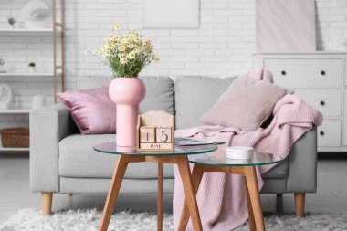 Oturma odasındaki masada papatya ve dergi bulunan küp takvimi.