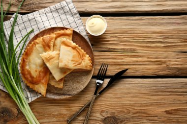 Lezzetli chebureks tabağı, ahşap masada yeşil soğan ve sos.