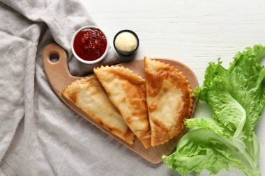 Lezzetli cheburekler, taze marul ve soslar beyaz ahşap masada.