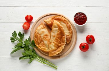Lezzetli cheburekler, domatesler, sos ve maydanoz beyaz ahşap arka planda, üst manzara
