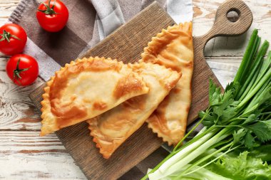 Hafif ahşap zemin üzerinde lezzetli chebureks, ot ve domates kompozisyonu