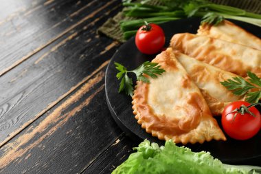 Lezzetli cheburekler, otlar ve domatesler koyu ahşap arka planda