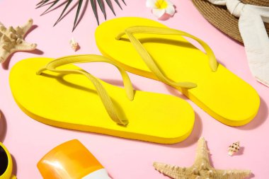 Pembe arka planda şık sarı parmak arası terlikler, yakın plan.