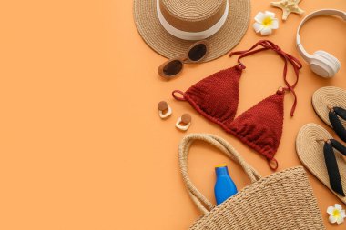 Turuncu arka planda şık bikinili ve plaj aksesuarlı kompozisyon, yakın plan.