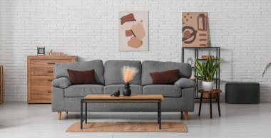 Rahat gri kanepesi ve beyaz tuğla duvarın yanındaki masası olan oturma odasının içinde.