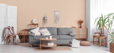 Oturma odasının iç tarafındaki bej duvarın yanında rahat bir kanepe, masa ve dergi tutucusu.