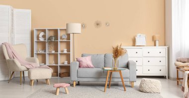 Oturma odasının içinde kanepe, koltuk ve raflar bej duvarın yanında.