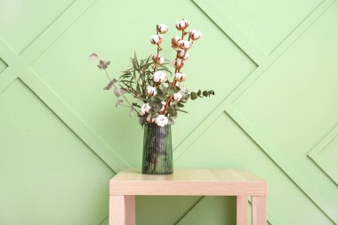 Pamuk filizi vazosu ve okaliptüs yeşil duvarın yanındaki açık ahşap masada.