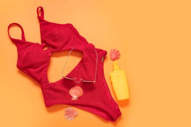 Şık bir mayo, güneş gözlüğü, bir şişe güneş kremi ve arka planda deniz kabuğu.