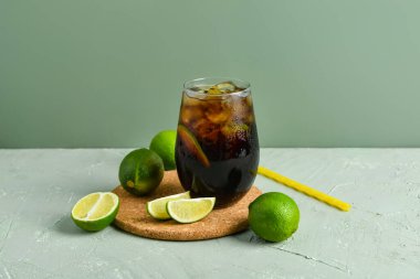 Bir bardak soğuk Küba Libre kokteyli ve gri arka planda limon.