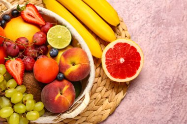 Pembe masada farklı taze meyvelerle dolu bir sepet.