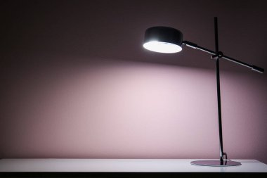 Karanlık odada bej duvarın yanındaki masada parlayan lamba.