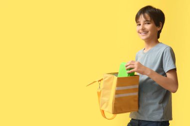 Sarı arka planda beslenme çantası olan küçük çocuk.