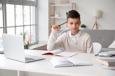Düşünceli küçük çocuk evde dizüstü bilgisayarla çalışıyor.