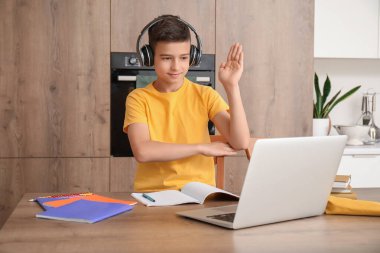 Kulaklık ve dizüstü bilgisayarı olan küçük çocuk mutfakta internetten ders çalışıyor.
