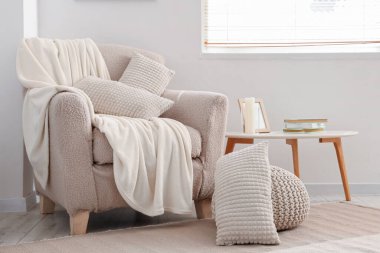 Hafif oturma odasının içinde yastıklı ve battaniyeli rahat bir koltuk.