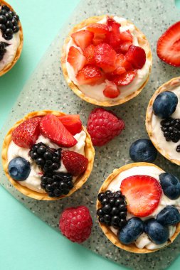 Krem şanti ve turkuaz arka planda böğürtlenli lezzetli tartlar.