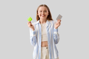 Prezervatifli genç bir kadın ve arka planda doğum kontrol hapları.