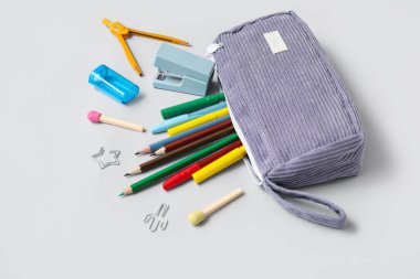 Gri arka planda farklı okul kırtasiyesine sahip mor kalem kutusu.