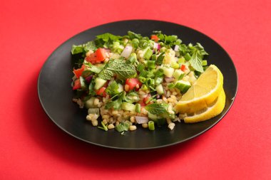 Lezzetli tabakta salata ve kırmızı arka planda limon dilimleri, yakın plan.