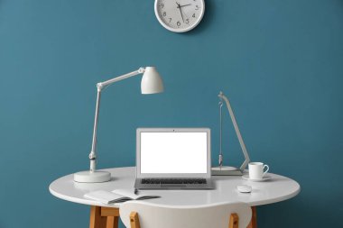 Modern dizüstü bilgisayarı, not defteri ve renkli duvarın yanında bir fincan kahvesi olan şık bir iş yeri.