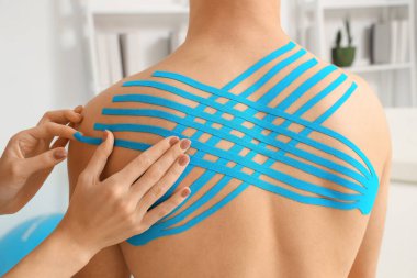 Rehabilitasyon merkezinde erkeğin sırtına bant yapıştıran kadın fizyoterapist.