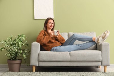 Evdeki kanepede uzanmış çay içen genç bir kadın.