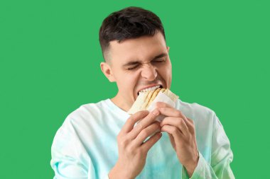 Yakışıklı genç adam yeşil arka planda lezzetli donör kebabı yiyor.