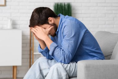 Evdeki kanepede oturan yorgun genç adam.