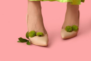 Pembe arka planda kasımpatı çiçekleri olan yüksek topuklu güzel genç bayanların bacakları.