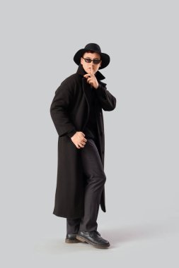 Kılık değiştirmiş erkek casus, arka planda sessizlik jesti gösteriyor.