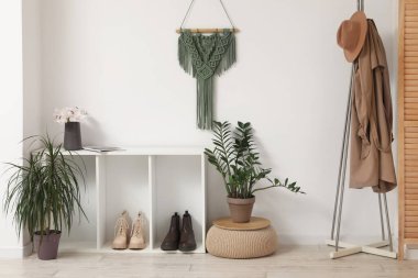 Beyaz duvarın yanında giysi rafı ve bitki örtüsü olan şık bir salon.