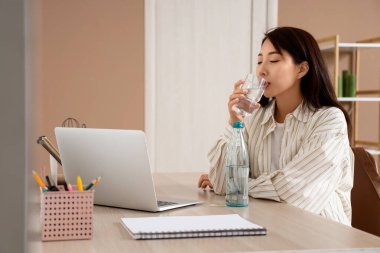 Ofiste su içen genç Asyalı kadın.