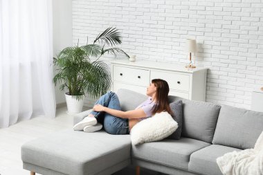 Oturma odasındaki rahat kanepede dinlenen güzel genç bayan.