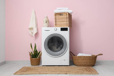 Çamaşırları, sepetleri ve pembe duvarın yanında bitkileri olan modern çamaşır makinesi.