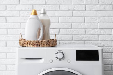 Beyaz tuğla arka planda deterjanları olan modern çamaşır makinesi, yakın plan.