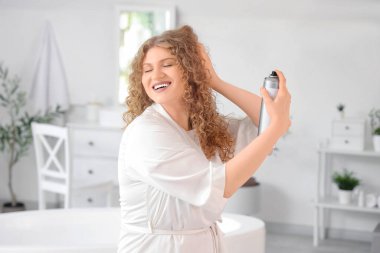 Evdeki banyoya saç spreyi sıkan genç ve güzel bir kadın.