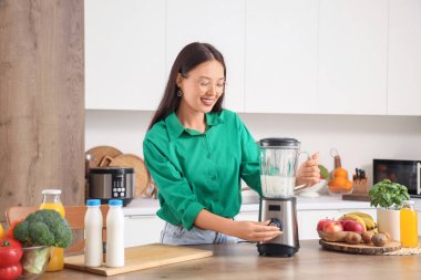 Genç Asyalı kadın mutfakta blender ile smoothie yapıyor.
