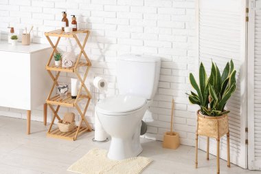 Beyaz klozet, raf ünitesi ve lavabolu çekmeceler tuvalette beyaz duvarın yanında.