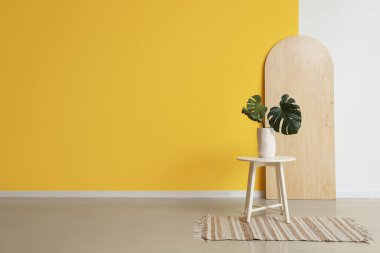 Sarı duvarın yanındaki masada vazo yaprakları vardı.