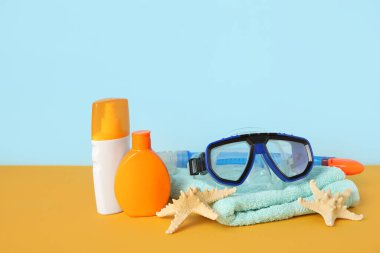 Havlu, güneş kremi şişeleri, yüzme maskesi ve arka planda yıldız balıkları, yakın plan.