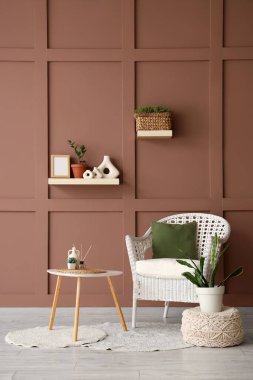 Masa, puf ve hasır koltuk, odanın içindeki kahverengi duvarın yanında.